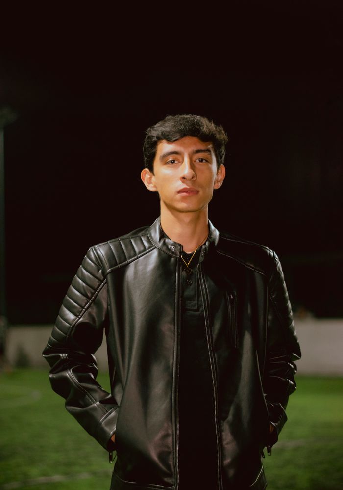A young adult wearing a black leather jacket standing outdoors at night.